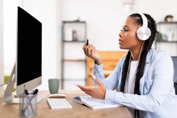 Örgülü Siyah Kadın Modern Kulaklıklar Takıyor Boş Bilgisayar Ekranına Bakarken — Stok fotoğraf