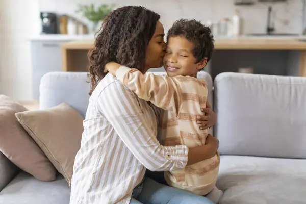 黑人妈妈一边坐在沙发上一边亲吻和拥抱年幼的儿子 快乐的非洲裔美国妈妈和呆在家里的男婴 妈妈和孩子享受彼此的时光 — 图库照片
