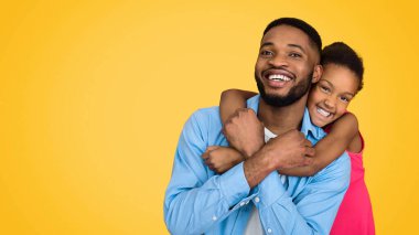 Küçük Afrikalı-Amerikalı kız kucaklama baba, sarı arka plan üzerinde eğleniyor