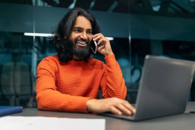Doğulu girişimci sakallı milenyum adamı akıllı telefondan iş görüşmesi yapıyor, karanlık ofis içlerindeki masada oturuyor, dizüstü bilgisayar klavyesine yazı yazıyor. İş dünyasındaki modern teknolojiler