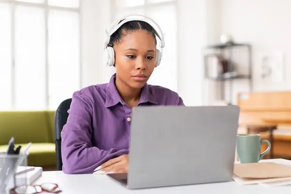 严重的非洲裔美国少女 在家庭环境中戴着白色耳机 用笔记本电脑看着屏幕 表现出专注和专注 — 图库照片