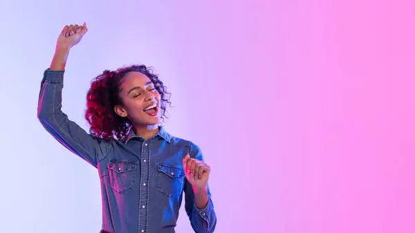 目を閉じたカーリー髪のラディアント黒人女性 デニムシャツで踊り ネオンピンクと紫色の勾配の背景 パノラマ 無料スペースでビートを感じる — ストック写真