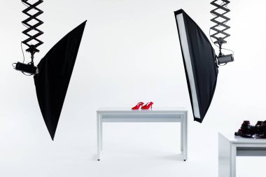 Profesyonel ışıklandırma ekipmanlarıyla modern fotoğraf stüdyosu. Temiz beyaz masa üzerinde canlı kırmızı topuklu ayakkabılar yakalamaya hazırlanıyorlar.