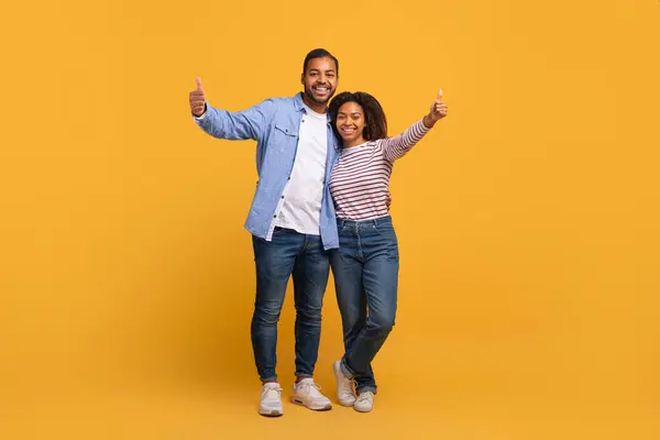 stock image Great Choice. Portrait of happy black couple gesturing thumbs up at camera, cheerful african american man and woman showing sign of approval while standing together over yellow background, copy space