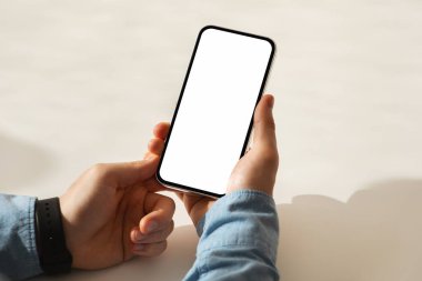 Mavi kot gömlek ve siyah akıllı kaset giyen, akıllı telefonu elinde tutan birinin elleri, teknoloji kullanımını veya mobil iletişimi öneriyor, kırpılmış, kapatılmış