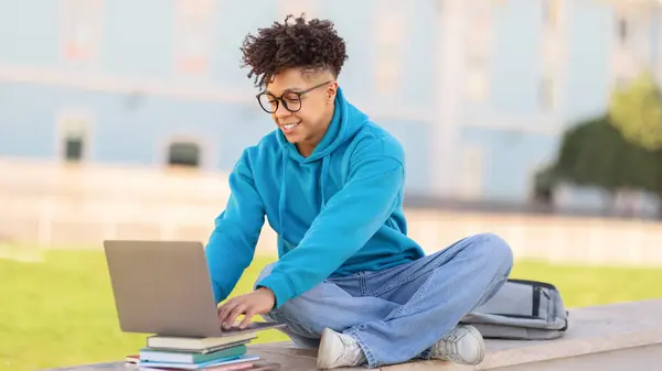 オンラインスタディ 笑顔の黒人の学生がノートパソコンでウェブをタイプして閲覧し 大学のキャンパスで屋外に座ることを学びました テクノロジーと大学教育 Eラーニングの概念 パノラマ — ストック写真