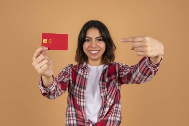 Orta doğulu genç bir bayan öğrenci elinde kırmızı plastik banka kredi kartını gösteriyor ve gülümsüyor, renkli bir geçmişi var. Temassız ödeme, tasarruf, depozito