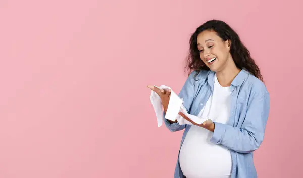 母亲的概念 快乐的孕妇 大肚子 手里拿着婴儿用品 面带微笑 情绪化 期待着孩子 粉红的工作室背景 复制空间 — 图库照片