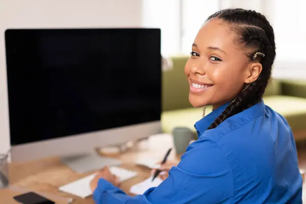 ハッピーブラックティーン女性学生Eラーニングコースを楽しんで 空白のコンピュータ画面で机に座って 明るい家庭環境でメモを取って カメラで笑顔 — ストック写真