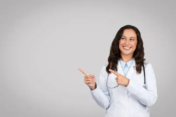 Beyaz Önlüklü Mutlu Genç Bayan Doktor Boş Yeri Işaret Ediyor — Stok fotoğraf
