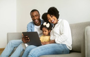 Aile İçin Çevrimiçi Boş Zaman. Mutlu Afrikalı Ebeveynler ve Çocuk Kızları dizüstü bilgisayar kullanıyor, internete bakıyor ve evdeki koltukta oturup çizgi film izliyor. Birlikte Hafta Sonu Kavramı