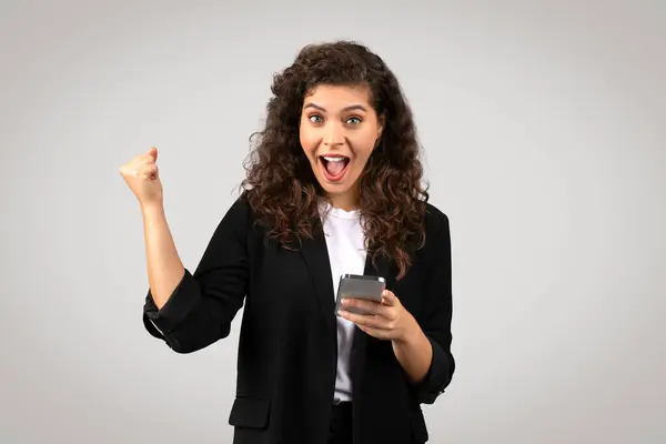 Ekscytująca Młoda Bizneswoman Kręconymi Włosami Trzymająca Smartfona Wykonująca Triumfalną Pompę — Zdjęcie stockowe