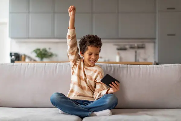 Vreugdevolle Zwarte Jongen Houden Smartphone Het Verhogen Van Zijn Arm — Stockfoto