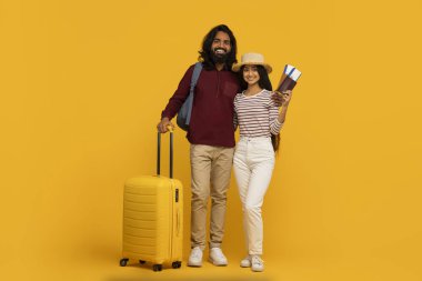 Mutlu bir seyahat çifti pasaportları ve sarı bir bavulla güneşli sarı bir arka planda duruyor.
