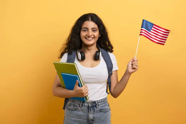 バックパックを持っている若い女性は アメリカの旗と笑顔を持って旅行や交換プログラムを示唆しています — ストック写真