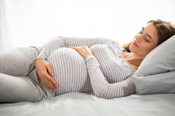 Piękna Młoda Kobieta Ciąży Obejmująca Brzuch Leżąc Łóżku Sypialni Uśmiechnięta — Zdjęcie stockowe