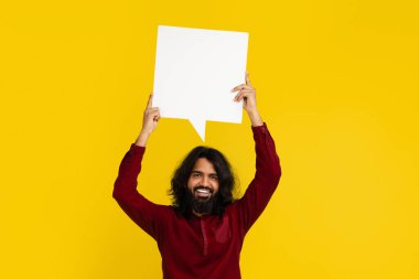 Neşeli, genç, yakışıklı, sakallı, beyaz, boş bir konuşma balonu tutan Hintli adamın portresi. Renkli sarı stüdyo arkaplanındaki yazı için boş bir alan.
