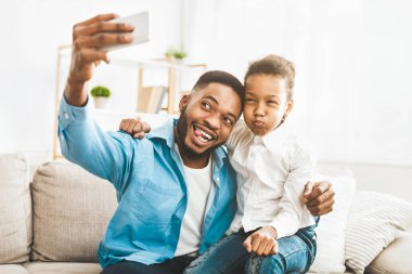 Aile zamanı. Mutlu bir afro baba, tatlı kızıyla kanepeye oturup selfie çekiyor.