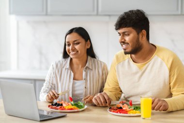 Neşeli genç Hintli çift kahvaltı edip film veya dizüstü bilgisayar başında podcast izliyor, eşler öğle yemeği yiyor ve bilgisayardan haberleri kontrol ediyor,