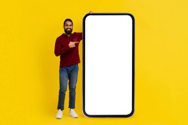 Havalı sakallı milenyum doğulu adam beyaz ekranlı akıllı telefonu işaret ediyor. Mobil uygulama reklamı için fotokopi alanı var.