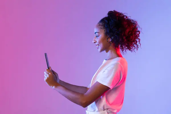 快乐的黑人妇女 卷曲的头发与她的平板电脑 轮廓与柔和的转换粉红到紫色霓虹灯背景 侧面看 — 图库照片