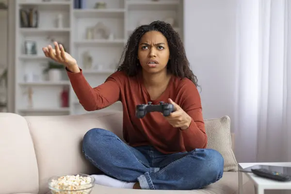 ストレスを受けた若い黒人女性とジョイスティックでリビングルームのインテリアで家に座って アフリカ系アメリカ人の女性が手で文句を言うとジェスチャー ビデオゲームでの苦しみの失敗 — ストック写真