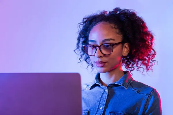聚精会神的年轻女性 戴着眼镜 靠着梯度照明在笔记本电脑上工作 — 图库照片