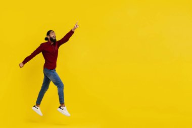 Heyecanlı, sakallı, genç Hintli hippi, sarı stüdyo arka planında izole edilmiş, fotokopi alanına bakıyor, harika bir online teklif sunuyor, ya da inanılmaz bir uzunluk.