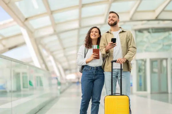 Havalimanı Terminalinde Bavul Akıllı Telefonla Bekleyen Mutlu Genç Bir Çiftin — Stok fotoğraf