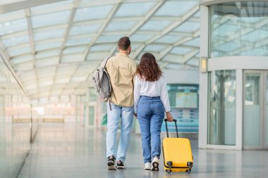 Birlikte seyahat ediyoruz. Havalimanında bekleyen genç bir çiftin, modern terminalde bekleyen ve el ele tutuşan sevecen erkek ve kadının, tatil gezisine hazır olup,
