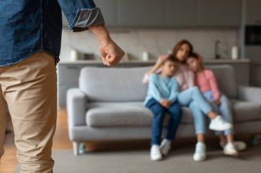 Aile içi şiddet. Tanımlanamayan bir adam karısını ve çocuklarını yumruğuyla tehdit ediyor, annesi ve kızını kucaklarken koltukta birlikte oturuyor, seçici bir şekilde erkek eline odaklanıyor.