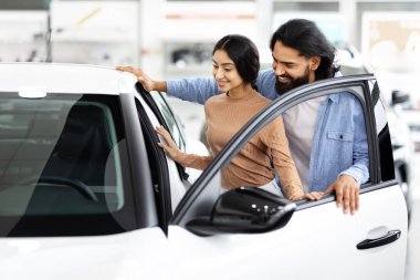 Mutlu bir Hintli çift, yeni bir beyaz arabayı galeride birlikte inceliyor.