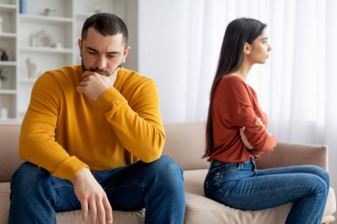Yetişkin bir erkek ve dişi ayrı bir kanepede oturuyor çatışma ya da anlaşmazlık belirtileri gösteriyor, üzgün ve dalgın görünüyor.