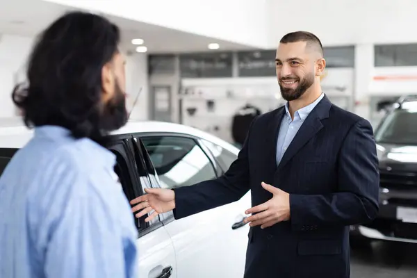一位穿着西装的专业汽车推销员在一家汽车经销店的陈列室里与一位潜在的印度客户约会 — 图库照片