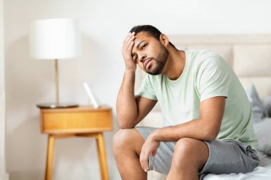 Afro-Amerikan bir adamın yatağın kenarına oturup, kafaya dokunduğu ve fotokopi çekilen yere baktığı düşünceli bir an.