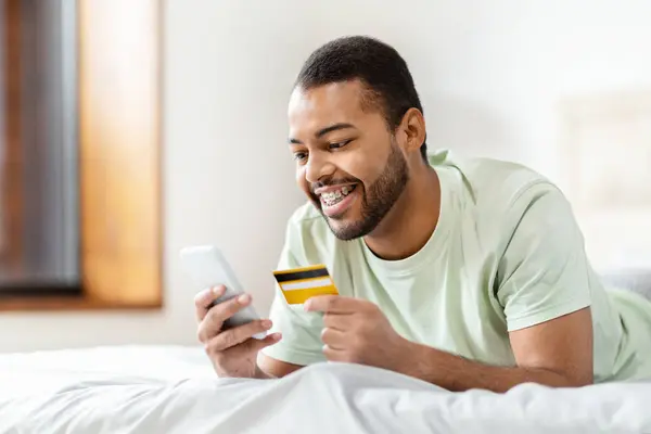 Joven Afroamericano Sosteniendo Una Tarjeta Crédito Mirando Teléfono Inteligente Probablemente —  Fotos de Stock