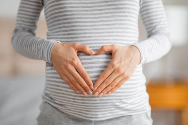 Close-up of a pregnant woman forming a heart shape with her hands on her striped shirt covering the belly clipart