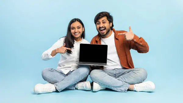 楽しい若いインドのカップルは カジュアルな座って 空のスクリーンで現代のPcのラップトップを指摘し 青いスタジオの背景に対して素敵なオンラインオファーやウェブサイトをお勧めします パノラマ モックアップ — ストック写真