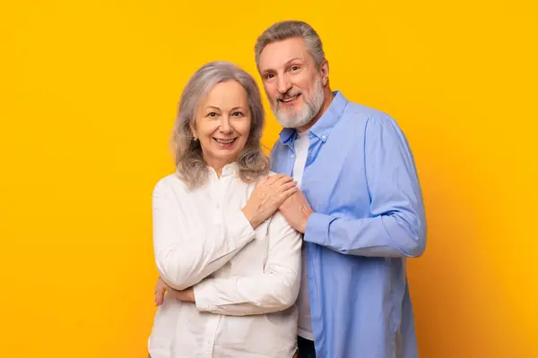 stock image Romantic bond. Affectionate happy senior couple showcasing the joy of lasting love and togetherness, embracing tenderly against yellow studio backdrop, smiling to camera. Good relationship concept