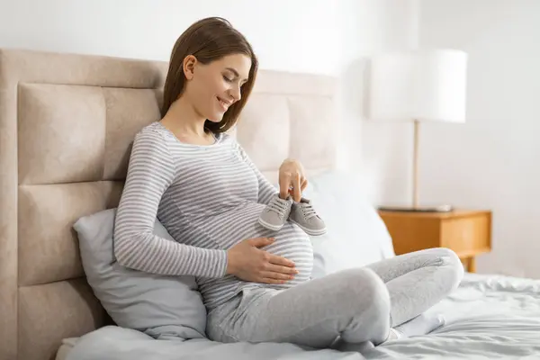 Joyful Expectant Mother Striped Shirt Holds Tiny Shoes Her Belly — Stock Photo, Image