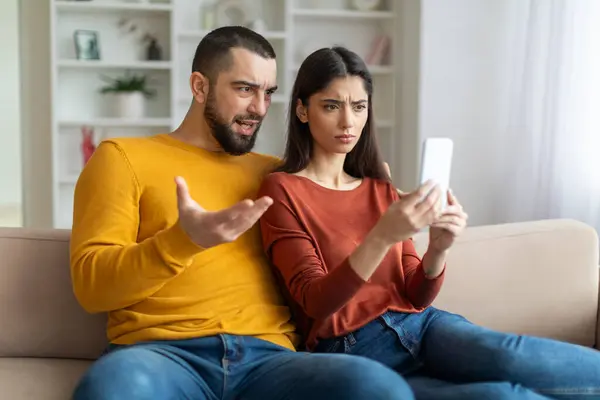 一对陷入困境的夫妇专注于智能手机 他们的表情暗示了他们的担忧或震惊 — 图库照片