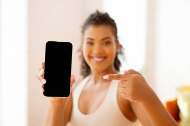 Genç sporcu bayan telefonunun boş ekranını gösteriyor, fitness uygulamalarının modelini gösteriyor, teknolojinin füzyonunu gösteriyor ve aktif yaşam tarzında, içeride poz veriyor. Seçici odak