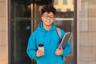 İçerik Brezilyalı erkek öğrenci kahve ve akademik ciltler taşıyor, şehir ortamında bir okul gününe hazır.