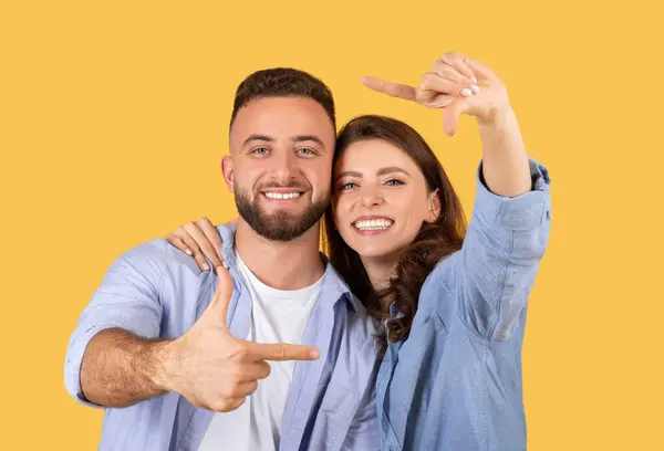 陽気な若いカップルは指でフレームを作り 黄色の背景に微笑みました — ストック写真