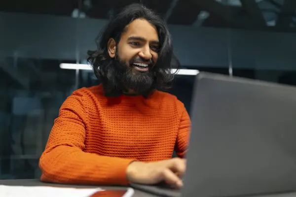 Man with a warm smile sitting comfortably while using his laptop in an office