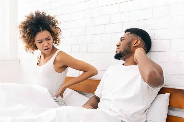 Uncomfortable mattress. Young african-american couple waking up, suffering from back and neck ache after bad night in bed, free space