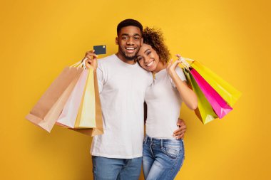 Alışveriş torbaları ve turuncu zemin üzerine kredi kartı ile çekici genç Afro-Amerikan çift