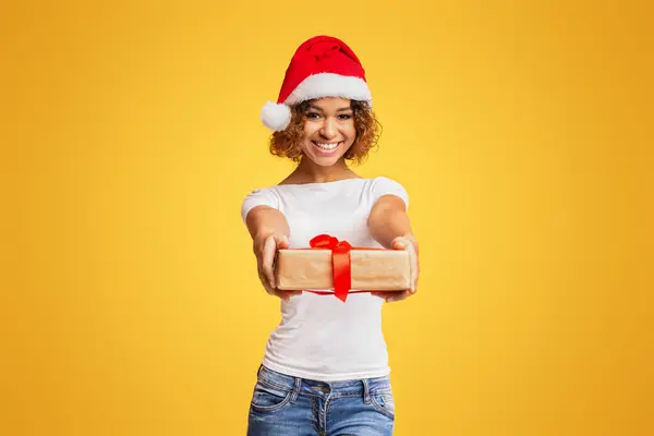 メリークリスマス カメラ オレンジの背景に休日のプレゼントボックスを与える陽気なアフリカ系アメリカ人の少女 — ストック写真