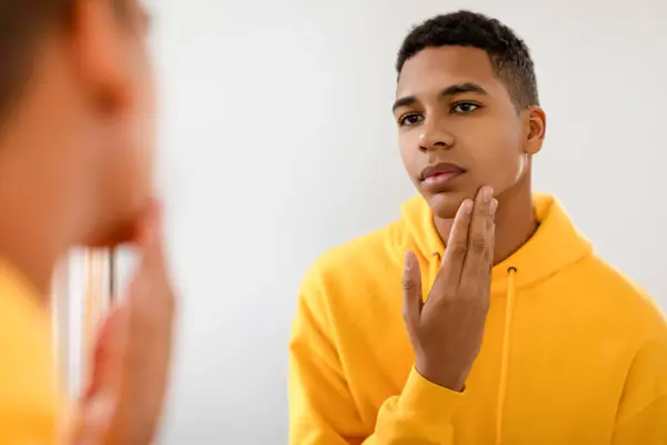 Sarı Kapüşonlu Düşünceli Genç Adam Aynada Tenini Inceliyor Parlak Minimalist — Stok fotoğraf