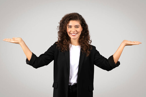 Профессиональная женщина в деловой одежде с приятной улыбкой делает балансирующий жест с ладонями лицом вверх